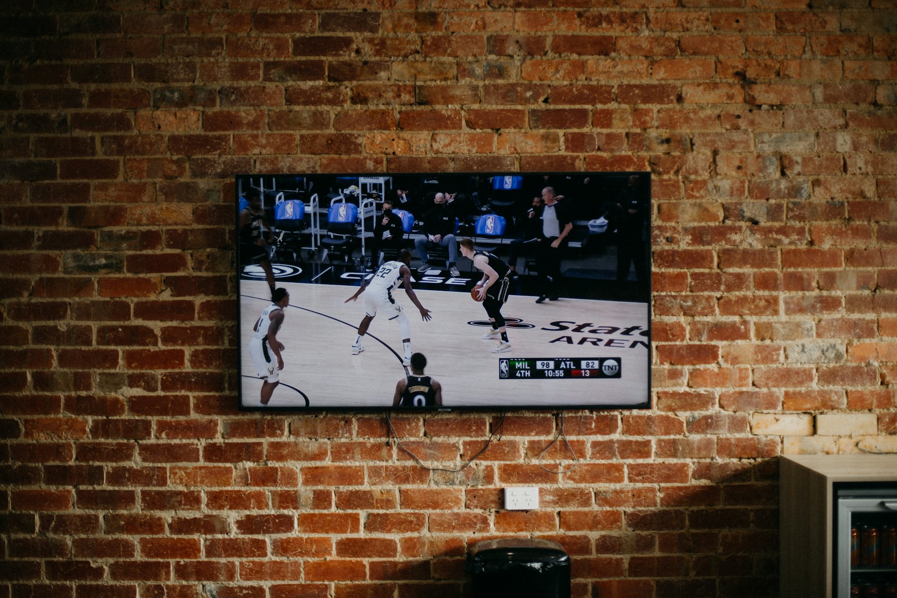 A flat-screen TV mounted on a warm brick wall in a bar